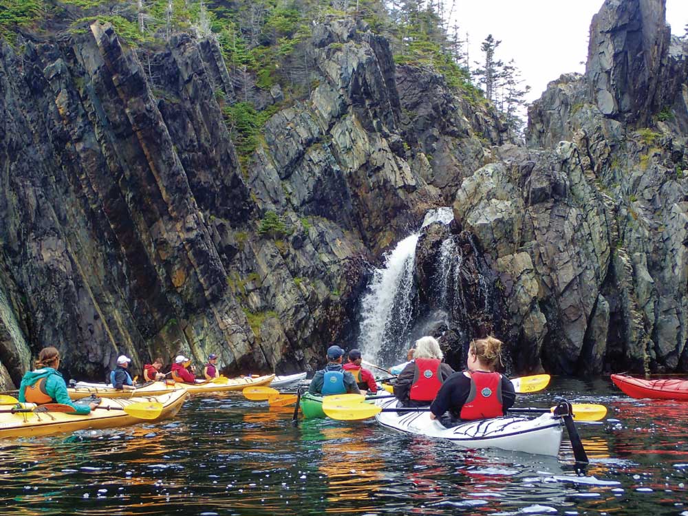 group of people sea kayaking in multiple kayaks on the water by large rocks