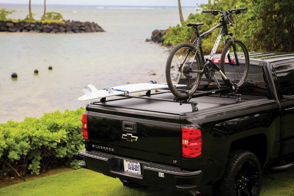 black pickup with bike rack with bike and surfboard parked on grass beside a lake