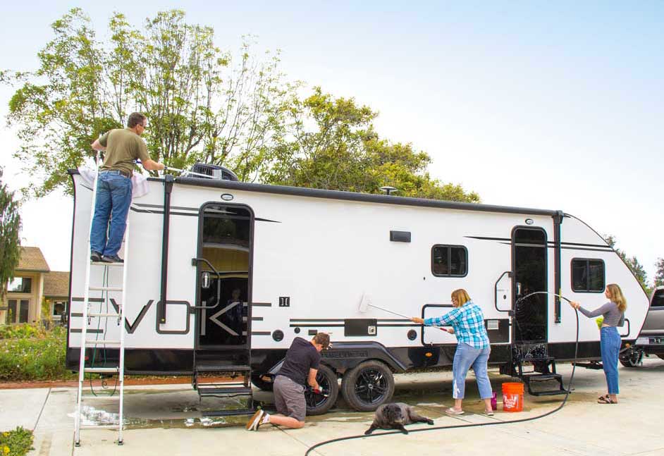 Four people washing a white travel trailer