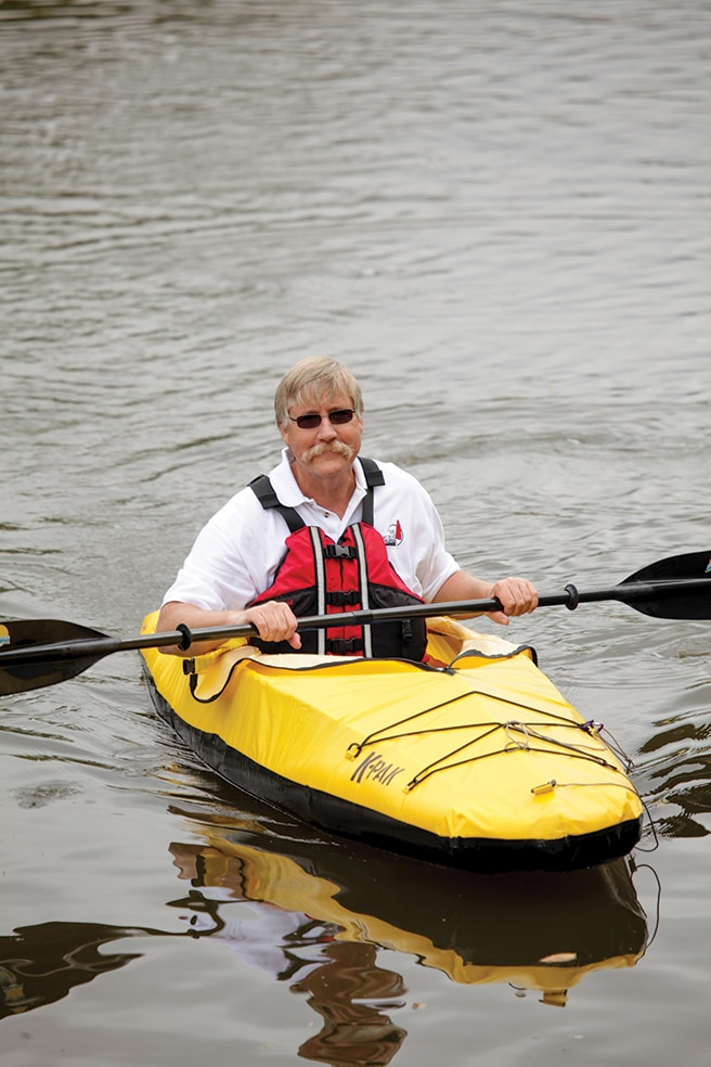 Older man with mustache in yellow kayak holding paddle on water