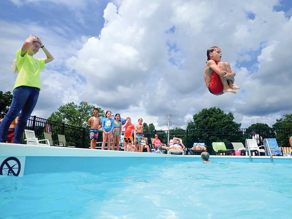 Woman wearing green shirt standing, looking at child doing cannonball in pool