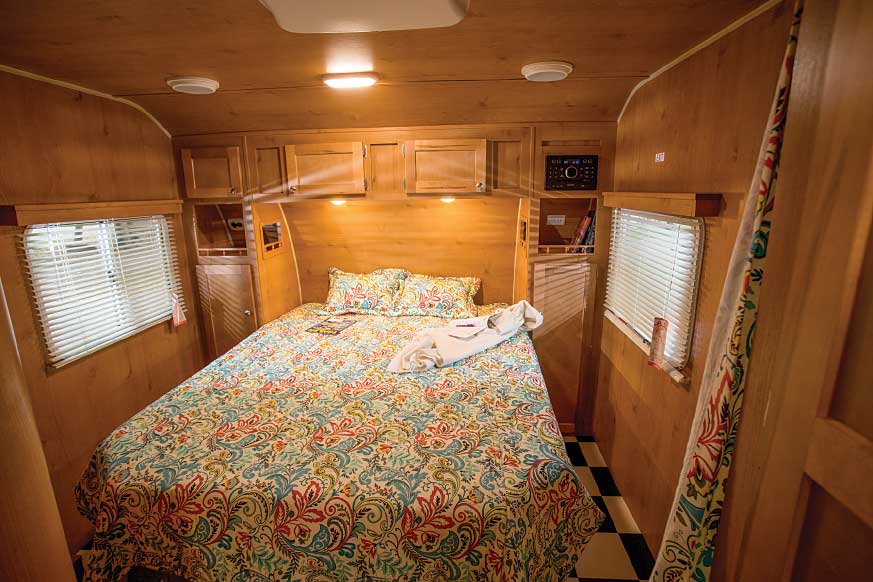 The bedroom offers overhead storage cabinets, plus shelves where power outlets are accessible from the walk-around queen bed. 