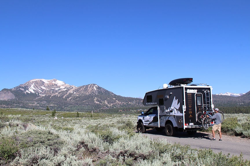 Truck camper with snow-covered Sierra Nevada mountains in background.