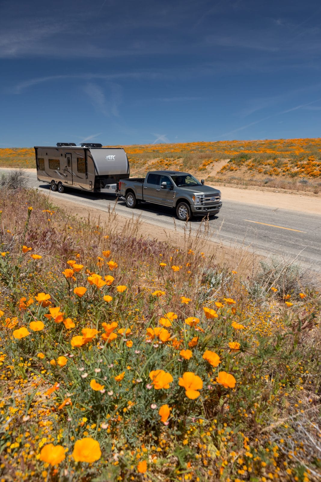 Silver Ford F-250 towing silver ATC 8528 on highway surrounded by orange poppies.