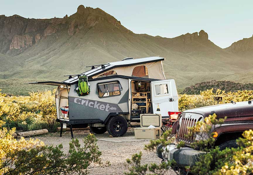 Cricket Overland trailer at rustic campsite with mountain ridge in background.