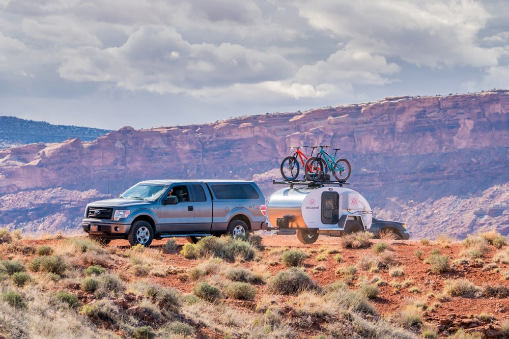 Truck pulling silver camper with bikes on top in desert