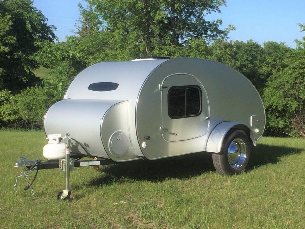 Tiny silver round travel camper parked on grass