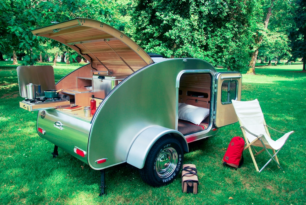 Shiny silver teardrop camper with back curved door open on green grass