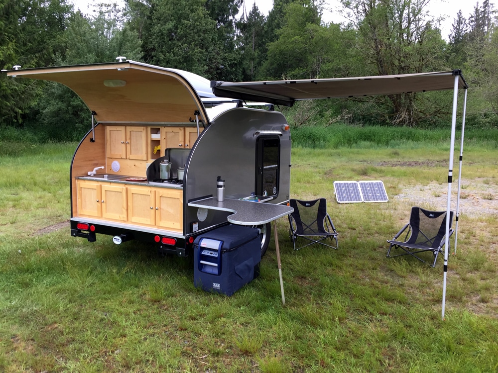 Silver teardrop camper with back door open and awning out