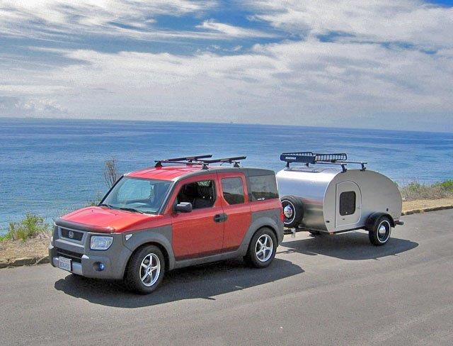 Red SUV pulling silver teardrop camper near water