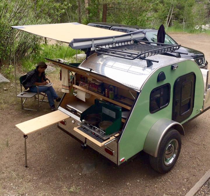 Green teardrop camper with awning and person sitting next to it outside