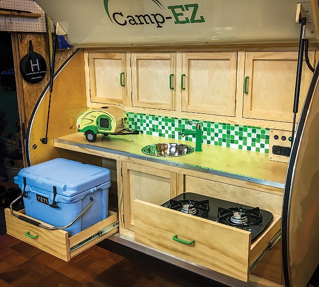 Rear of trailer with birch cabinets, blue cooler and drawer for stove.