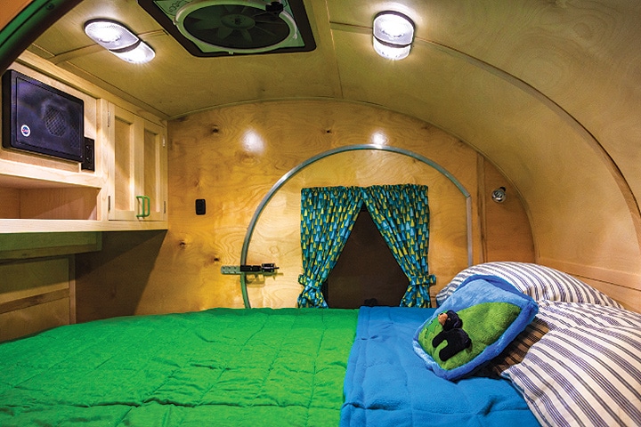 The bed takes up the inside space with a green bedspread, birch walls and two lights overhead.