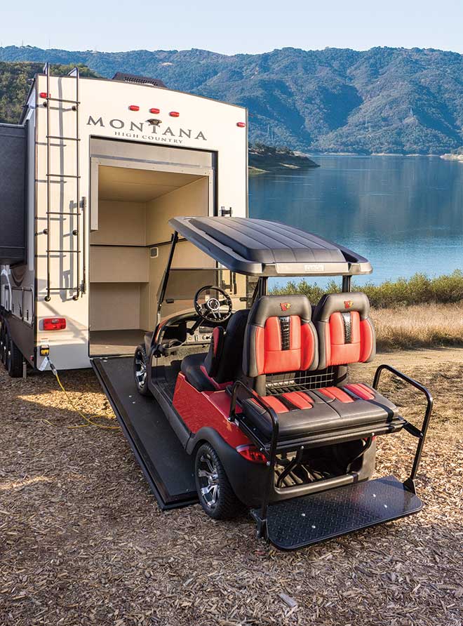 Golf cart on incline of door to back of Montana RV with lake in background