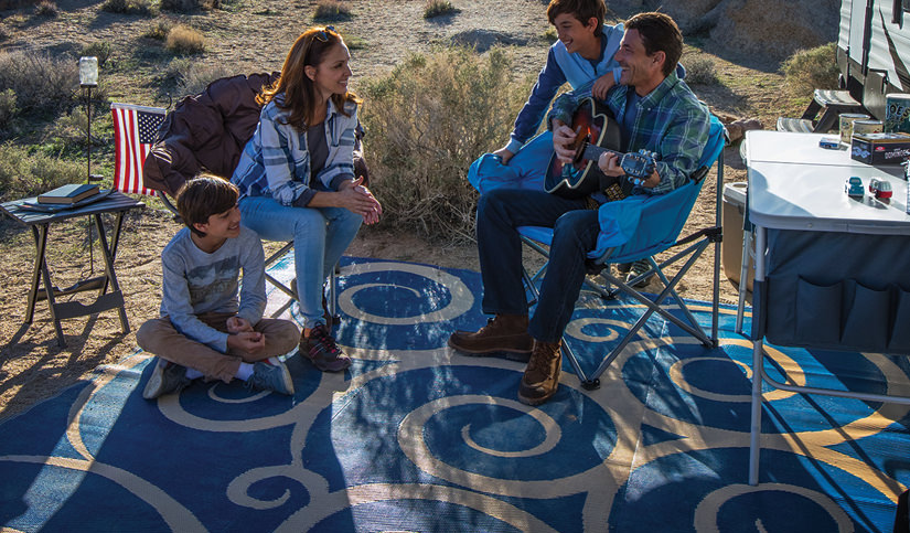 Family camping outdoors, sitting on outdoor rug father playing guitar