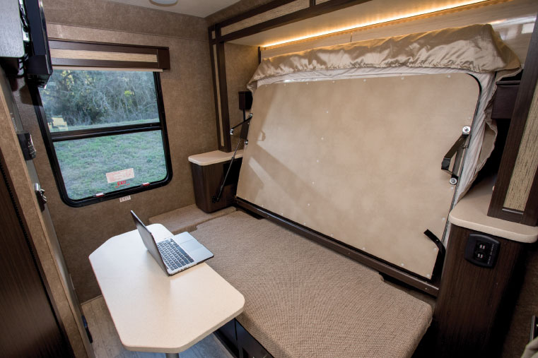 Beneath the folded bed, left, is a cushioned seating area and mounting point for the table, creating a workspace illuminated by the large window at the rear of the coach.