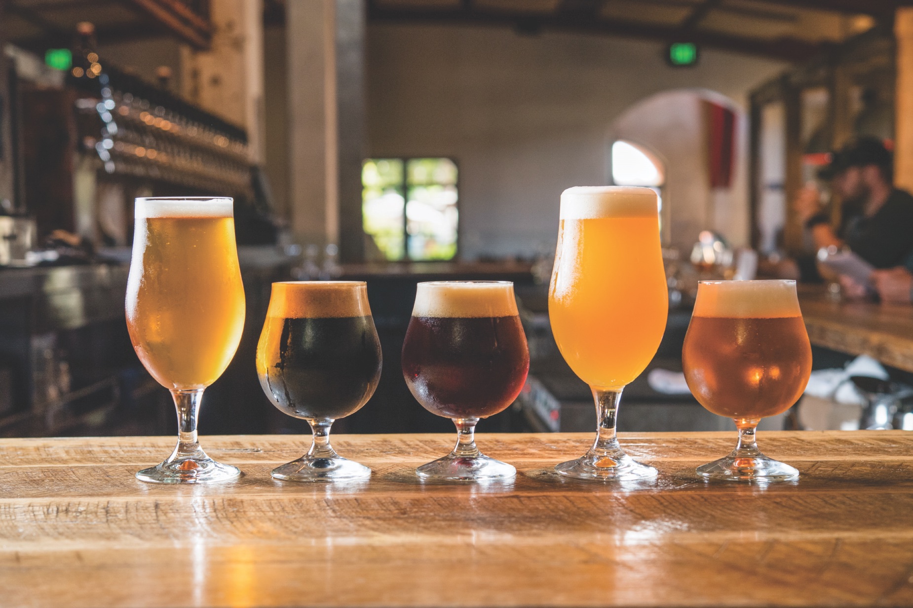 five different craft beers sitting on a bar.