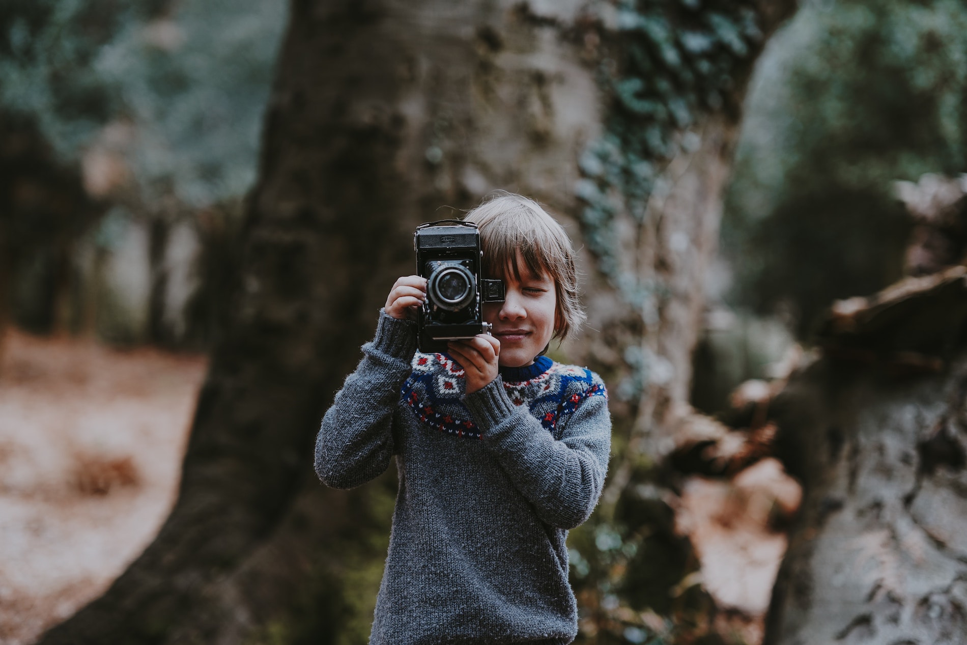 A Young boy taking a picture using an old camera