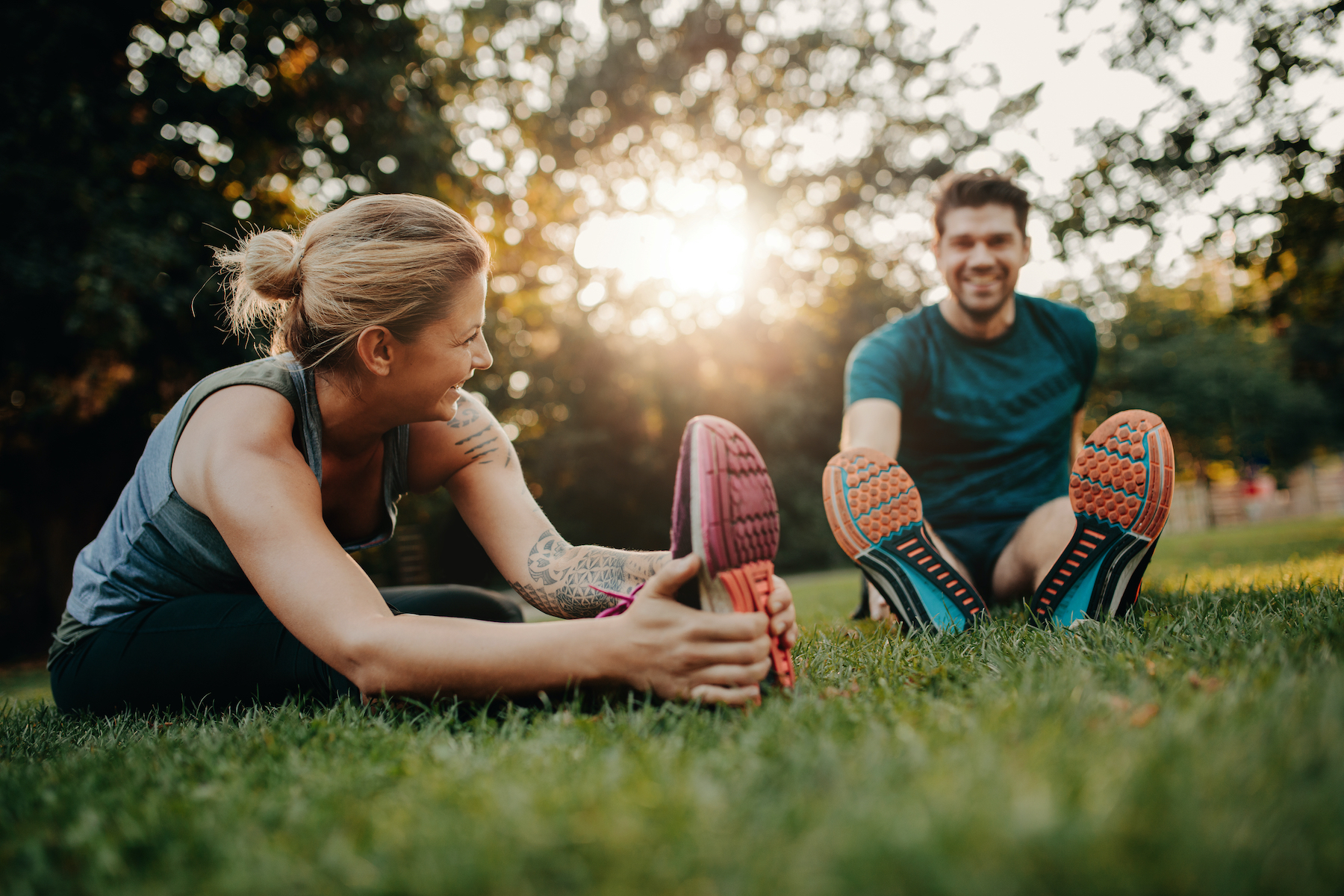 Fitness couple stretching outdoors in park. Young man and woman exercising together in morning.