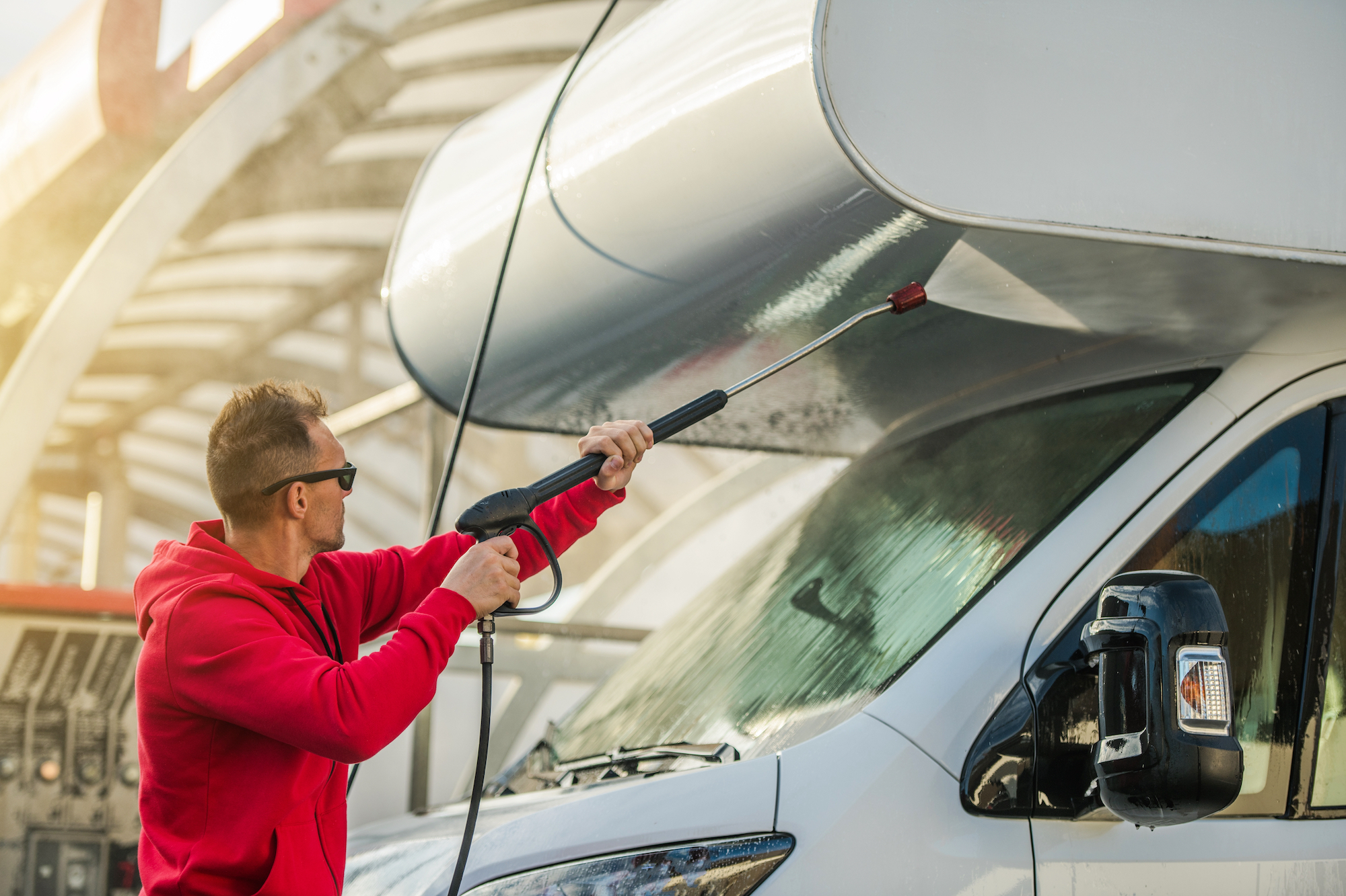 Seasonal RV Recreational Vehicle Motorhome Cleaning Using Pressure Washer. RV Camper Car Washing by Caucasian Men in His 30s.