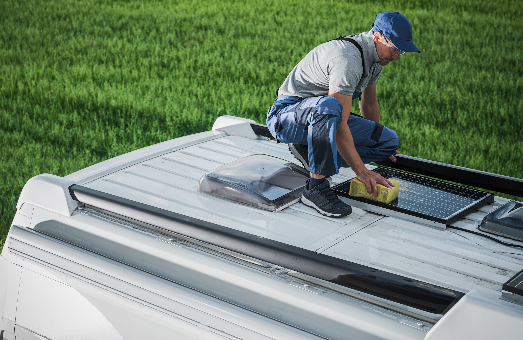 Caucasian Men in His 40s Cleaning Camper Van RV Roof Installed Solar Panels Using Sponge and Soft Washing Detergent. Motorhome Maintenance. RV Industry Theme.