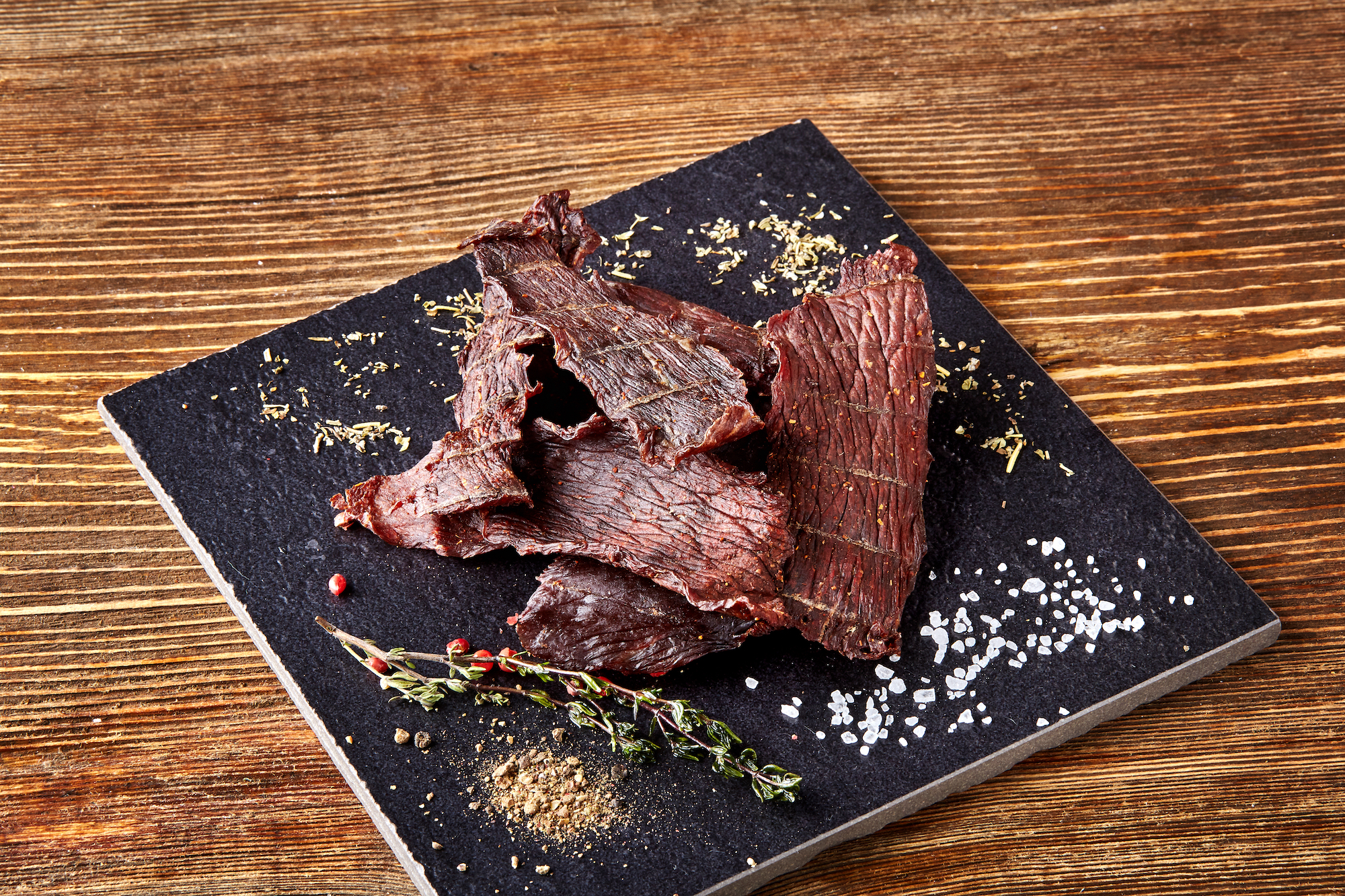 Dried peppered beef jerky cut in strips on the black board on wooden background