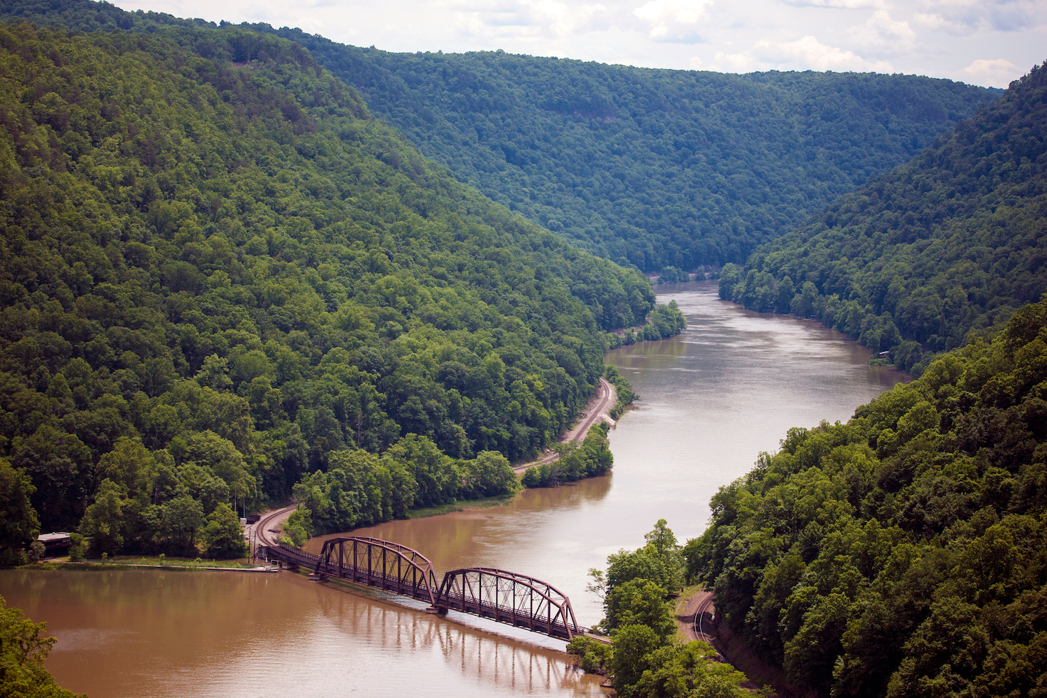 The graceful curves of the Gauley River in West Virginia with lush summer forest rising sharply from its' banks, a train tressel crossing near the bottom of the image.