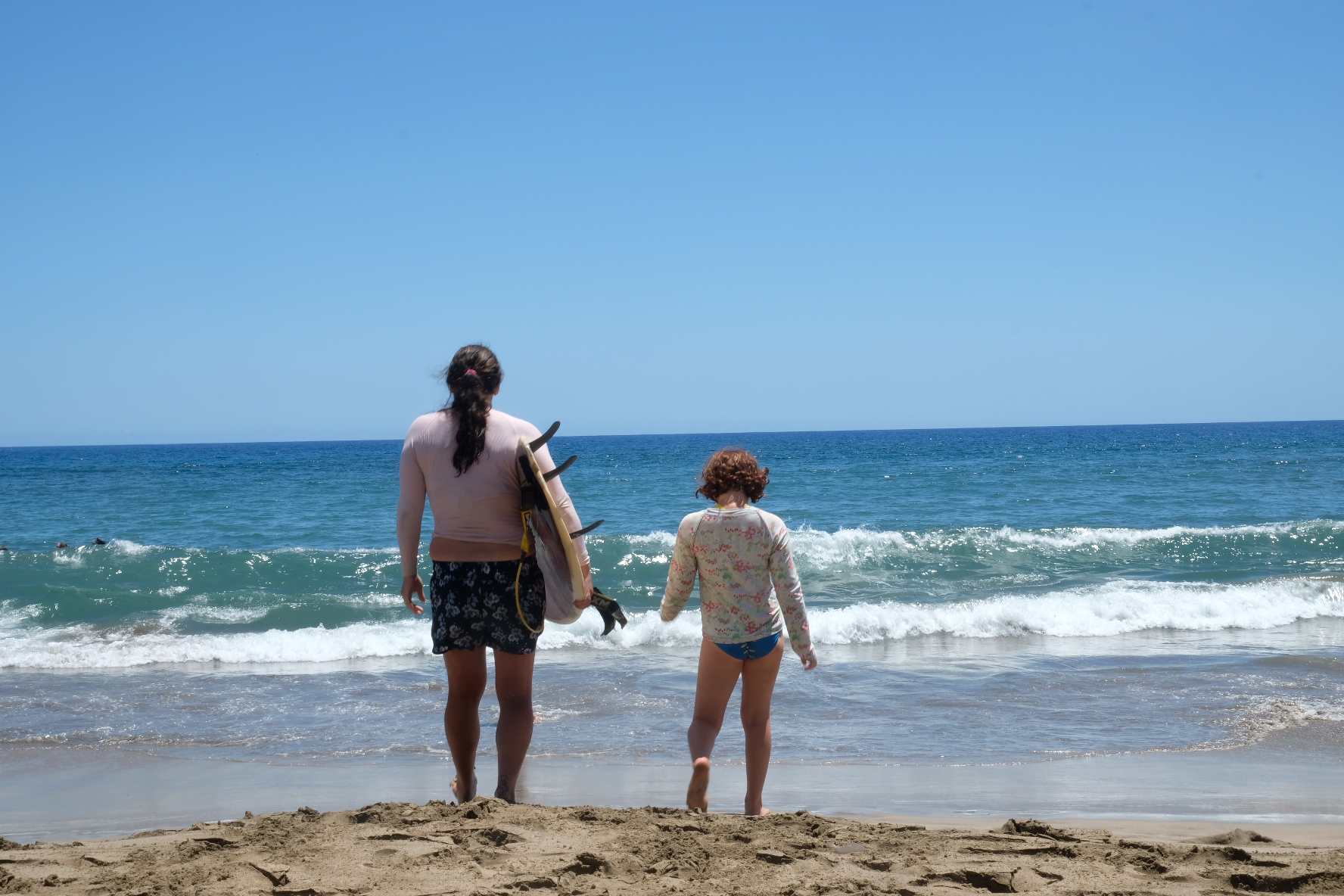 A mom heads out to the surf with her daughter.