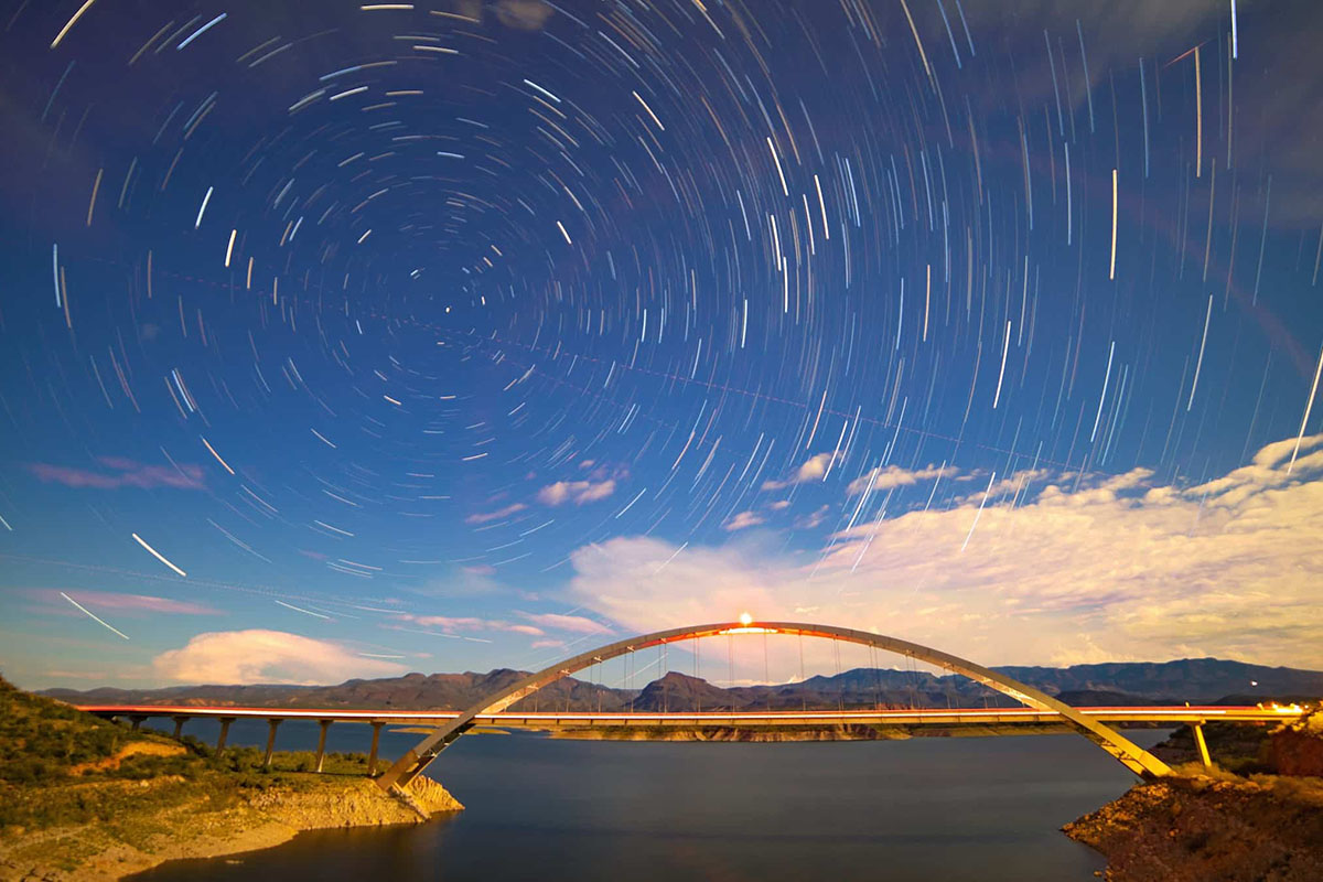 Arched bridge over lake with time-lapse stars.