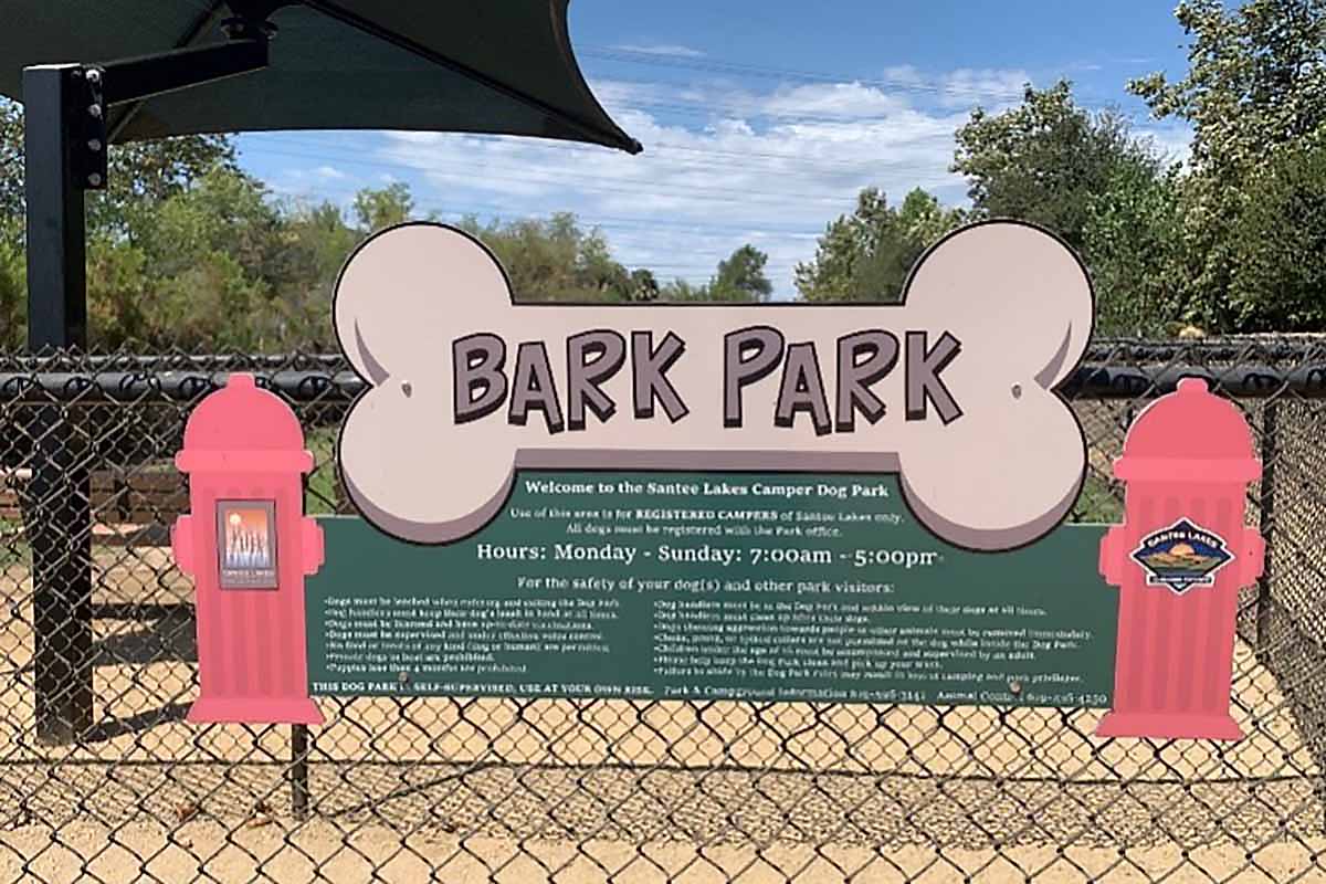 A fence with a sign proclaiming, "Bark Park."