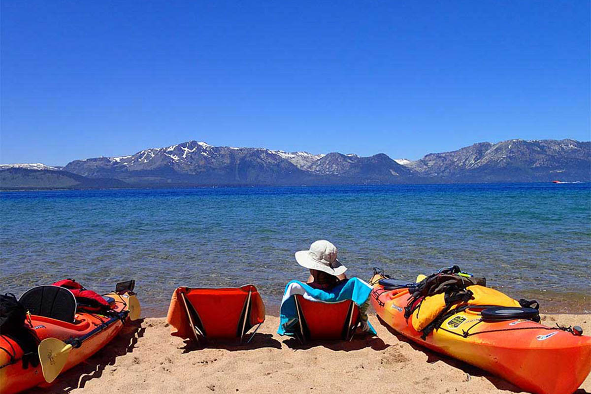 Person on a beach lounging with two kayaks.