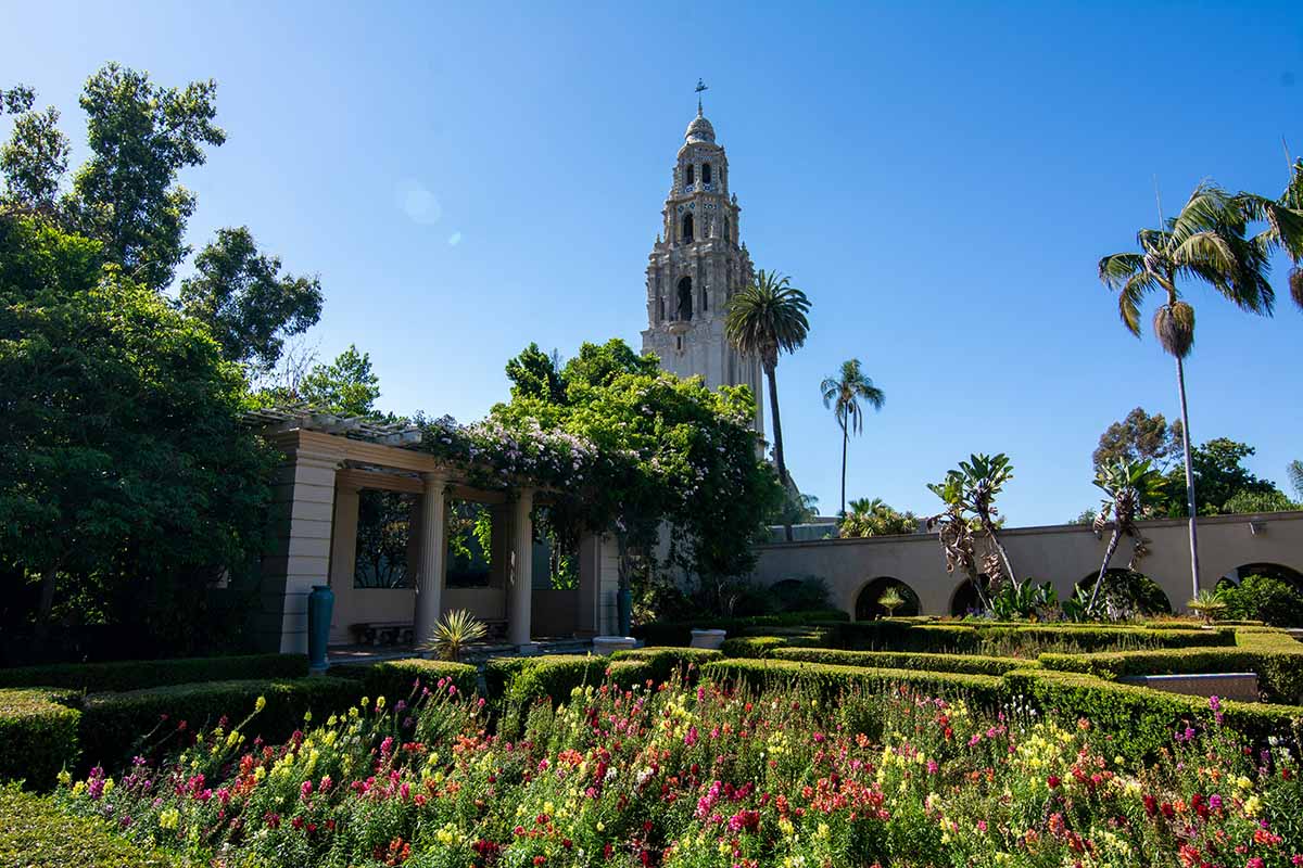 Elegant Spanish-style tower looms over a colorful garden and hedges.