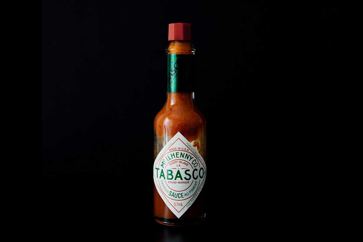 A bottle of Tabasco Sauce in a dark space.