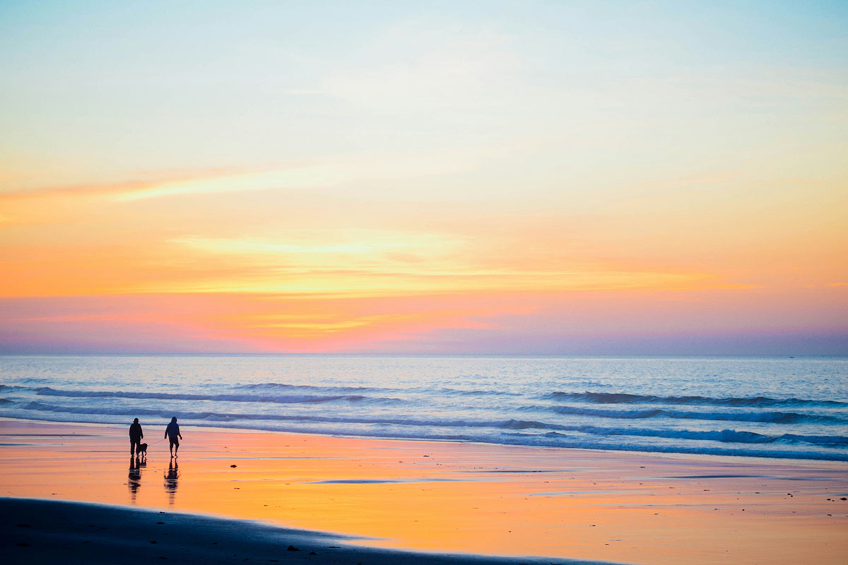A couple stroll a sunkist beach at dusk.