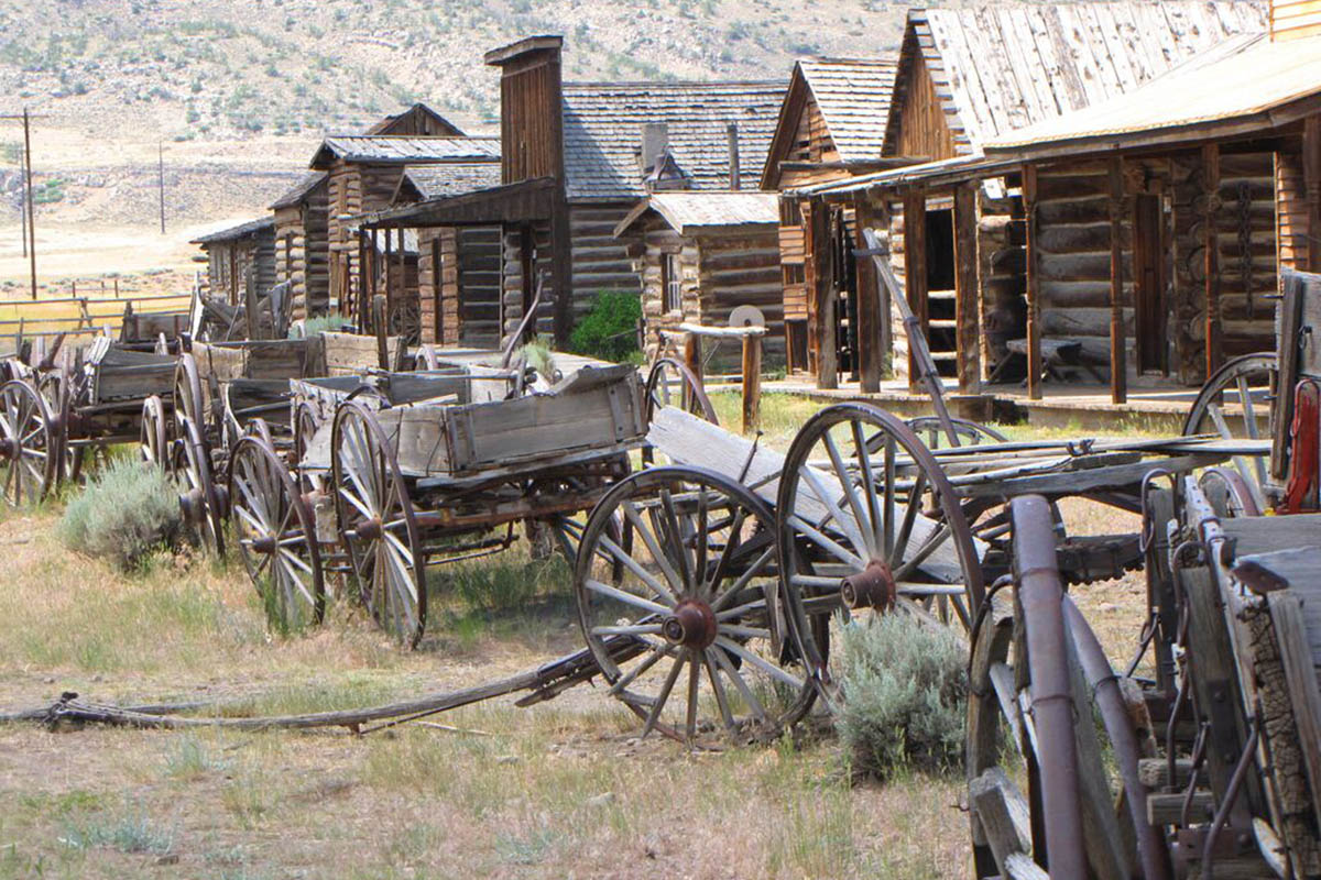A row of delapidated wagons in front of old wooden structures.