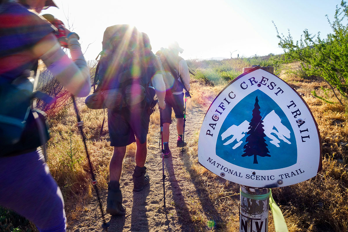Hikers traversing a wide trail with sign.