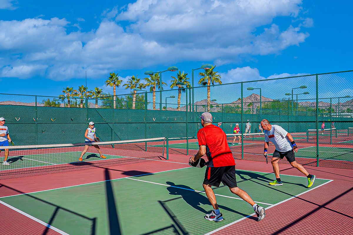 Doubles match pickeball under blue sky.