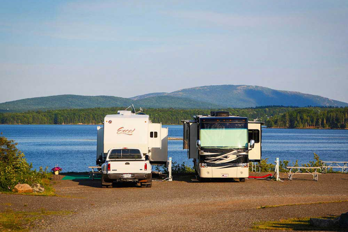 Motorhome and fifth-wheel parked near lake.